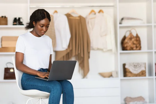 Serieuze zwarte dame met behulp van laptop typen zitten in garderobe kamer — Stockfoto