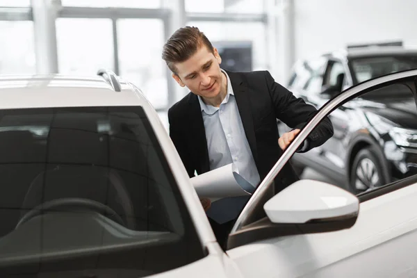 Satış merkezinde satmadan önce otomobili kontrol eden yakışıklı genç bir araba satıcısı — Stok fotoğraf