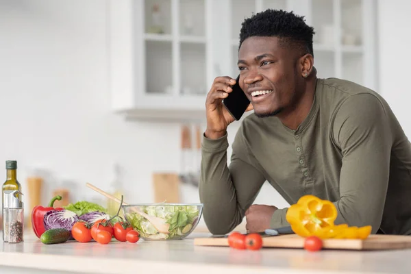 Comunicación móvil. Feliz hombre negro guapo hablando por teléfono celular en la cocina — Foto de Stock