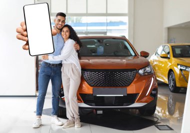 Güzel orta doğu çifti cep telefonlarını gösteriyor, yeni araba alıyorlar.