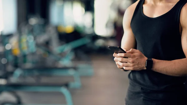 Кадр мускулистого человека, носящего умные часы со смартфоном в спортзале — стоковое фото
