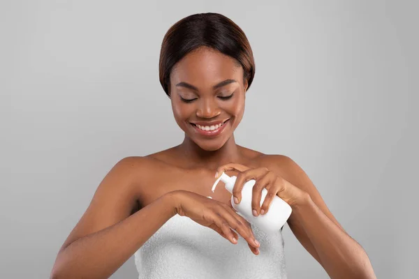Живлення тіла. Приваблива чорна жінка наносить зволожуючий лосьйон на руку — стокове фото