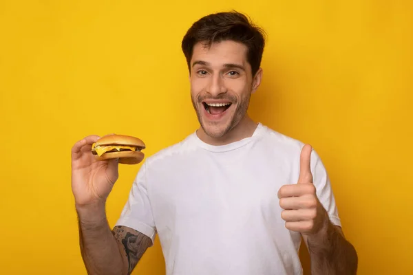 Cara engraçado segurando hambúrguer mostrando polegar para cima — Fotografia de Stock