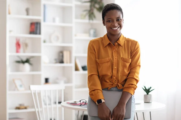 Mujer afroamericana bastante posando con portátil en la oficina —  Fotos de Stock