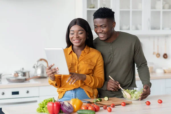 Cónyuges afroamericanos felices preparando comida en la cocina y usando tableta digital — Foto de Stock