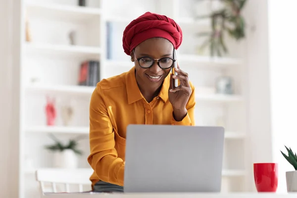 Afro-americano bisinesswoman avendo conversazione telefonica, controllando computer portatile — Foto Stock