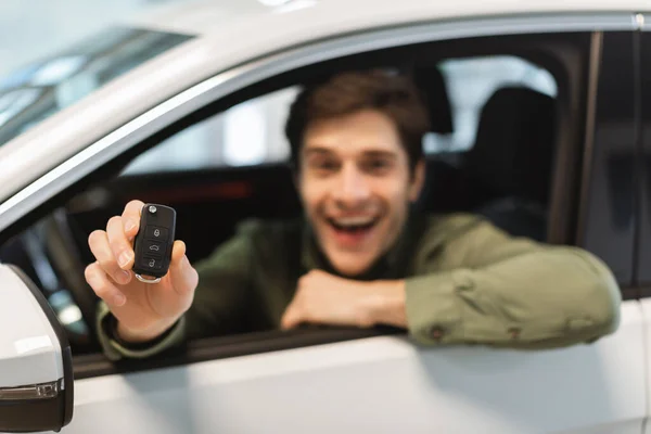 Vidám fiatalember kezében kulcs auto, vásárol vadonatúj autó bemutatóteremben, szelektív fókusz — Stock Fotó