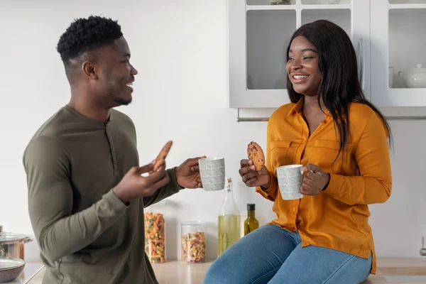 Loisirs en couple. Heureux conjoints noirs Boire du café avec des cookies dans une cuisine confortable — Photo