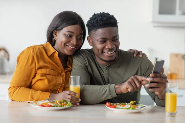 Glückliches afroamerikanisches Paar entspannt sich mit Smartphone beim Frühstück in der Küche — Stockfoto