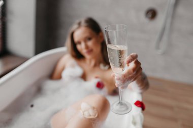 Köpüklü banyoda dinlenen ve elinde bir kadeh şampanya tutan bir kadın, elinde meşrubatla eline odaklan, yakın plan.