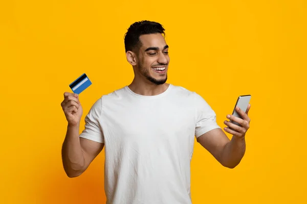 Pozytywny facet z Bliskiego Wschodu ze smartfonem i kartą kredytową — Zdjęcie stockowe