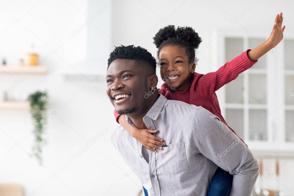 Happy black father piggybacking his pretty little daughter