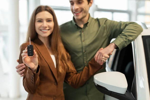 Feliz jovem casal caucasiano mostrando a chave para o seu novo carro na loja concessionária de automóveis, foco seletivo — Fotografia de Stock