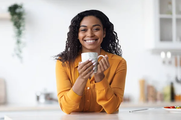 Cheerful african american lady drinking tea at home