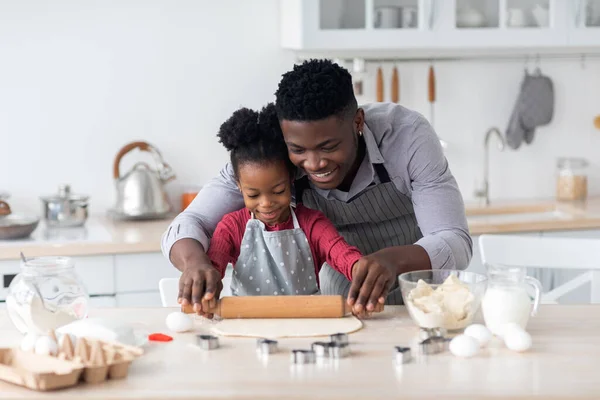 Kochający czarny ojciec piecze ciasteczka z małą córeczką, toczy ciasto — Zdjęcie stockowe