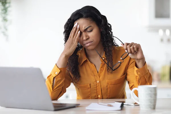 Erschöpfte schwarze Frau hat Kopfschmerzen, während sie von zu Hause aus arbeitet — Stockfoto