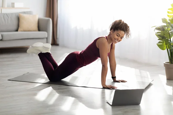 Привлекательный спортивный черный женщина упражнения дома, с помощью ноутбука — стоковое фото