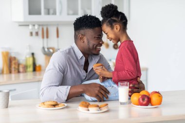 Mutlu siyah baba küçük kızına sarılıyor, mutfakta kaynaşıyor.