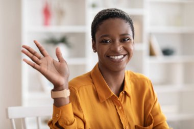 Mutlu siyah kadın evde poz veriyor, kameraya el sallıyor.