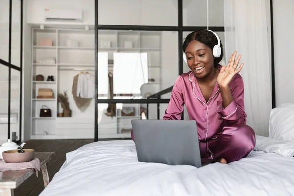 Fröhliches schwarzes weibliches Videotelefonat winkt Laptop im Schlafzimmer zu — Stockfoto