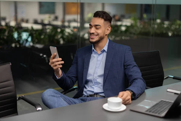 Alegre empresario árabe sentado en la mesa de trabajo, hablando por teléfono — Foto de Stock