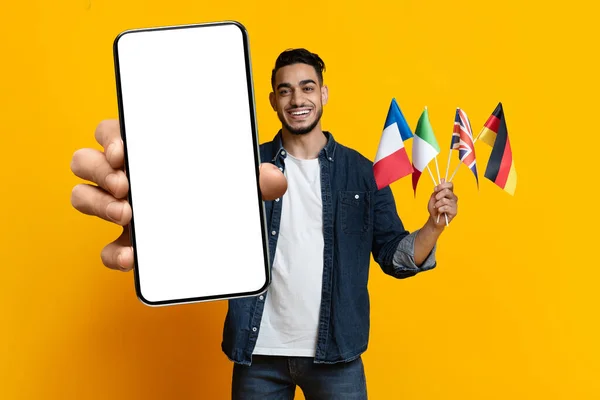 Positieve Midden-Oosterse student toont vlaggen en smartphone, mockup — Stockfoto