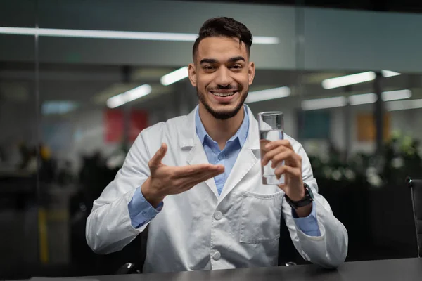 Cheerful middle eastern doctor holding glass of water