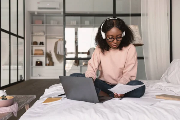 Afroamerikanerin sitzt mit Laptop-Lesepapier im Schlafzimmer — Stockfoto