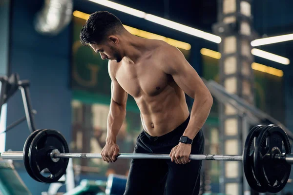 Мускулистый араб без рубашки поднимает тяжелую штангу во время тренировки в спортзале — стоковое фото