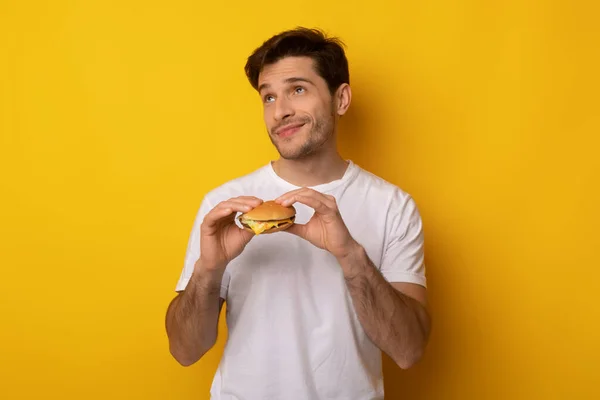 Divertido joven sosteniendo hamburguesa en el estudio — Foto de Stock