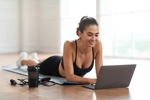 Ung dam som ligger på yogamattan med laptop-dator — Stockfoto