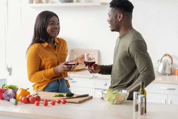 Feliz hombre negro y mujer beber vino mientras se prepara la comida en la cocina — Foto de Stock