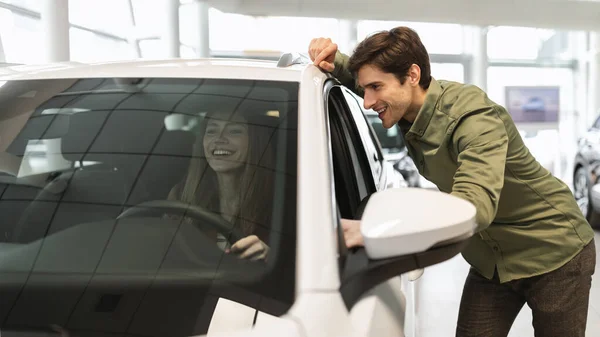 Joyful joven pareja caucásica comprobar nuevo coche de lujo antes de comprar en el salón de automóviles concesionario, diseño de la bandera — Foto de Stock