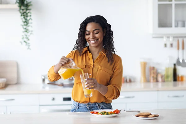 Lächelnde schwarze Frau schenkt frischen Orangensaft ein, Kücheneinrichtung — Stockfoto
