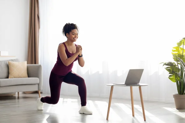 Черная женщина, имеющая онлайн фитнес-класс дома, с помощью ноутбука — стоковое фото
