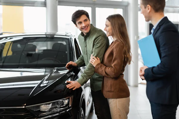 Bilköp eller biluthyrning. Millennial Kaukasiska par talar med försäljaren om att köpa ny bil hos återförsäljare — Stockfoto