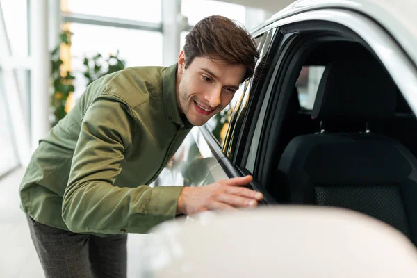 幸せな若い男彼の新しい車に触れて、ディーラーセンターで自動車を購入することに興奮し、スペースをコピー — ストック写真