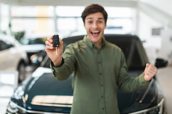 Jovem caucasiano animado mostrando a chave do carro novo na câmera, gesticulando SIM, comemorando a compra de automóvel na concessionária — Fotografia de Stock