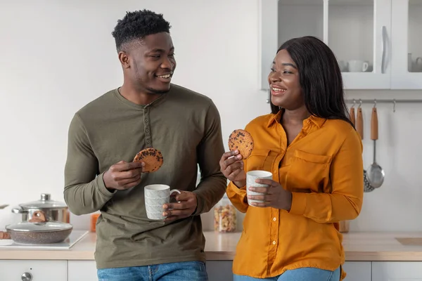 Retrato de feliz pareja negra bebiendo café y comiendo galletas en la cocina — Foto de Stock