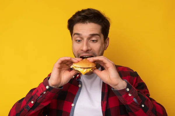 Divertido chico sosteniendo hamburguesa mordiendo sándwich en el estudio —  Fotos de Stock