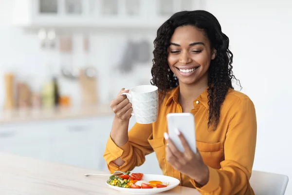 Glimlachende zwarte vrouw surfen op sociale media tijdens het ontbijt — Stockfoto