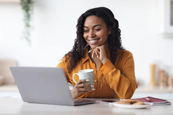 Joyeuse femme afro-américaine regardant un film sur ordinateur portable, buvant du café — Photo