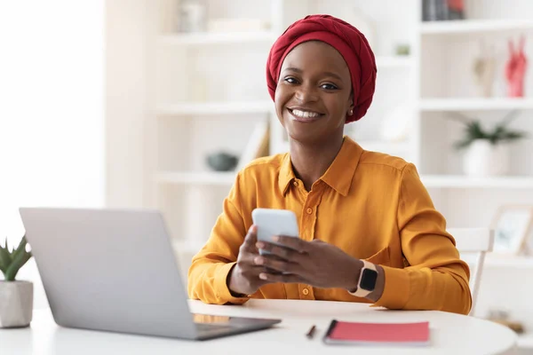 Empresária americana africana alegre usando smartphone e laptop — Fotografia de Stock