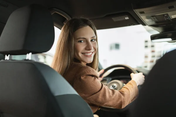 Glad ung vit kvinna köper ny bil, gör provkörning, sitter inne modern lyx auto på återförsäljare — Stockfoto
