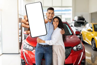 Olumlu Arap çift arabanın yanında duruyor, cep telefonlarını gösteriyorlar, maket yapıyorlar.