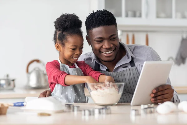 Очаровательный черный отец и дочь пекут вместе, используя цифровой планшет — стоковое фото