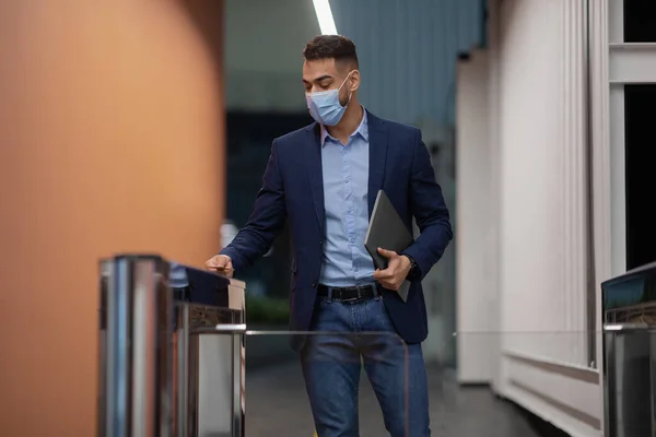 Empregado em máscara facial segurando laptop, passando pelo portão de entrada — Fotografia de Stock