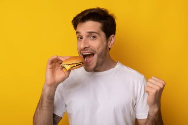 Gülümseyen genç adam stüdyoda Burger tutuyor.