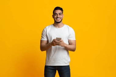 Cep telefonu kullanan neşeli Arap adam, sarı stüdyo geçmişi var.
