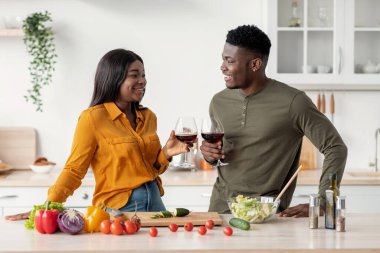 Sevecen siyah çift birlikte yemek hazırlarken mutfakta kırmızı şarap içiyor.